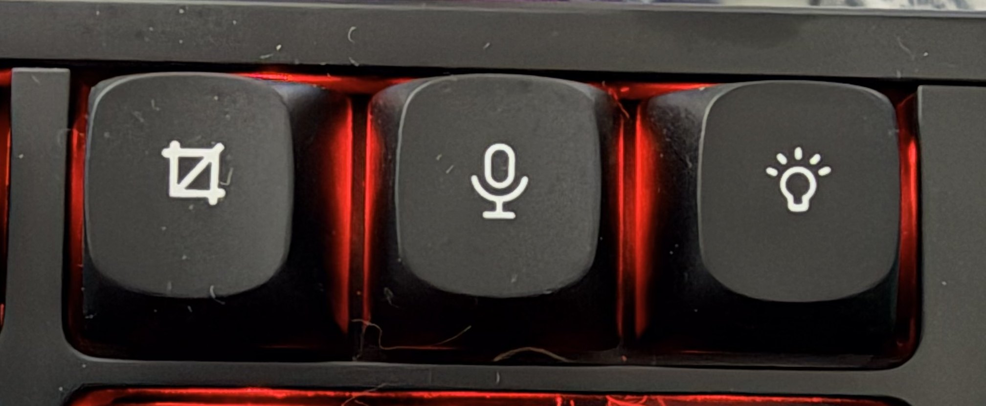 A close photograph of the three top-right utility keys on the physical keyboard: a screen capture icon, a microphone, and a light bulb, lit red by the stock effect.