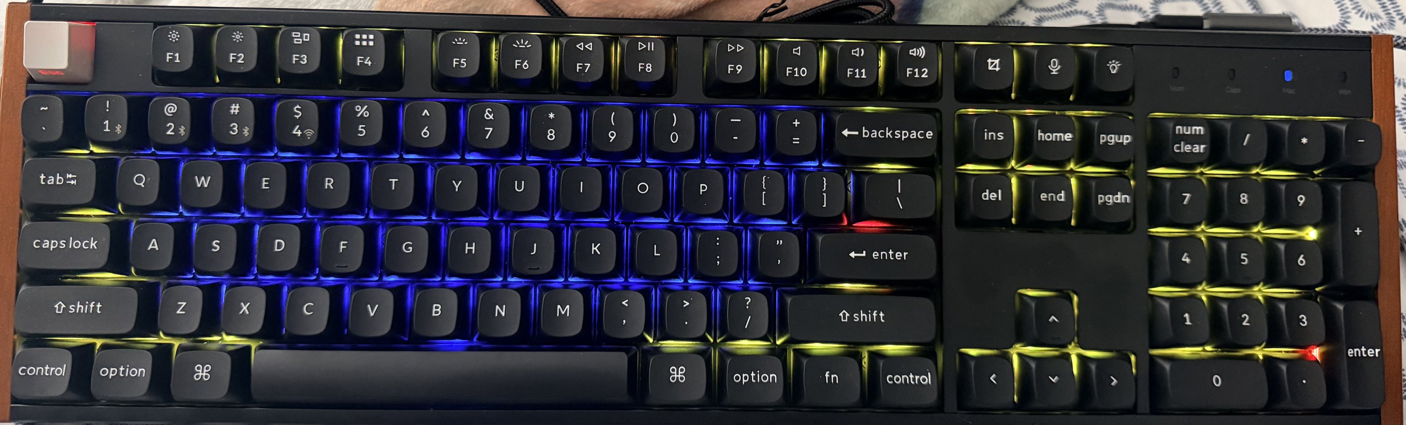 The physical Keychron K10 HE on the desk, every key lit in the factory rainbow effect: blue across the alphanumeric block, yellow-green through the function row and numpad, with one or two red keys.